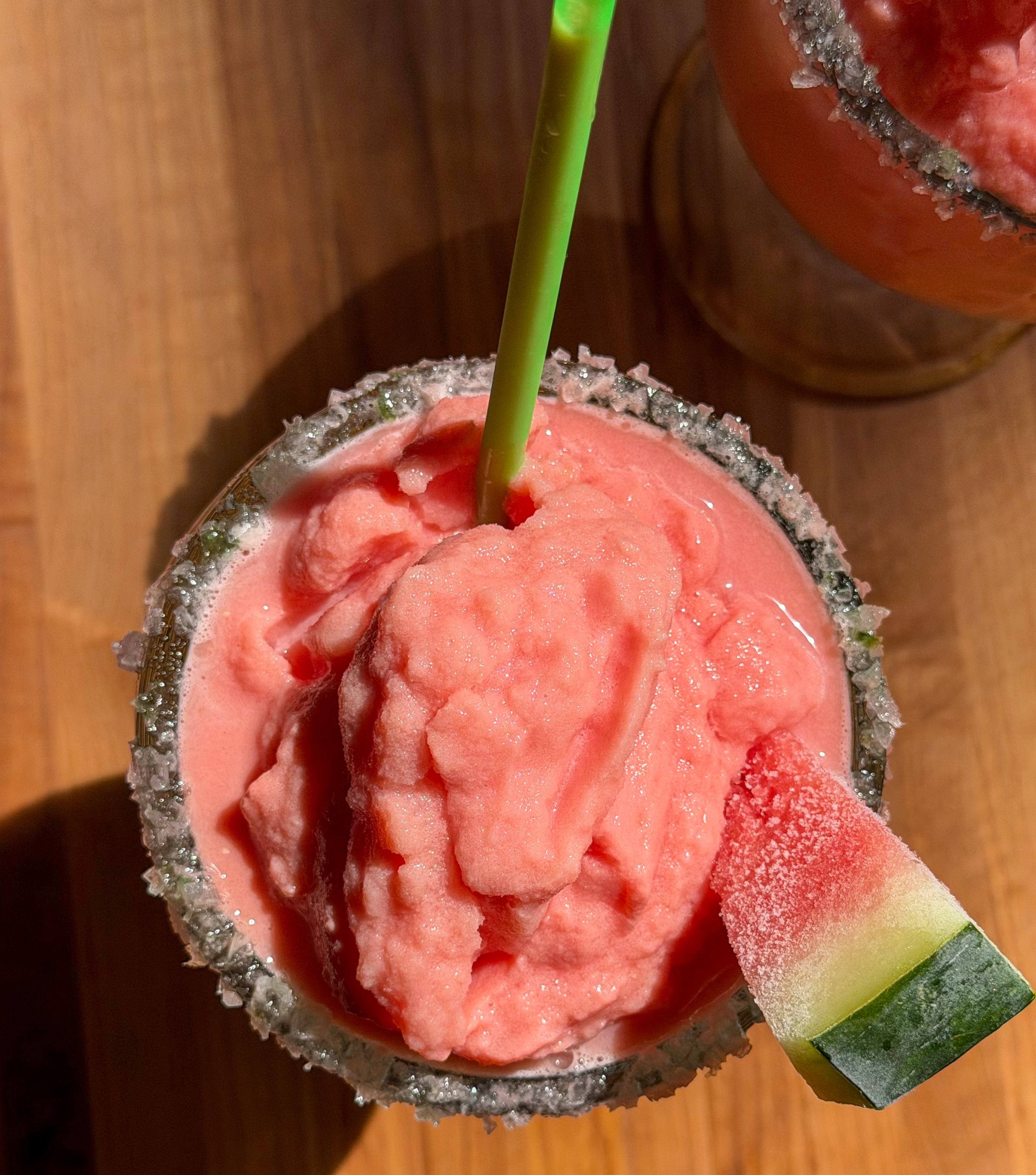 Watermelon margarita mocktail in a glass with a green sugar-salt rim and watermelon wedge garnish