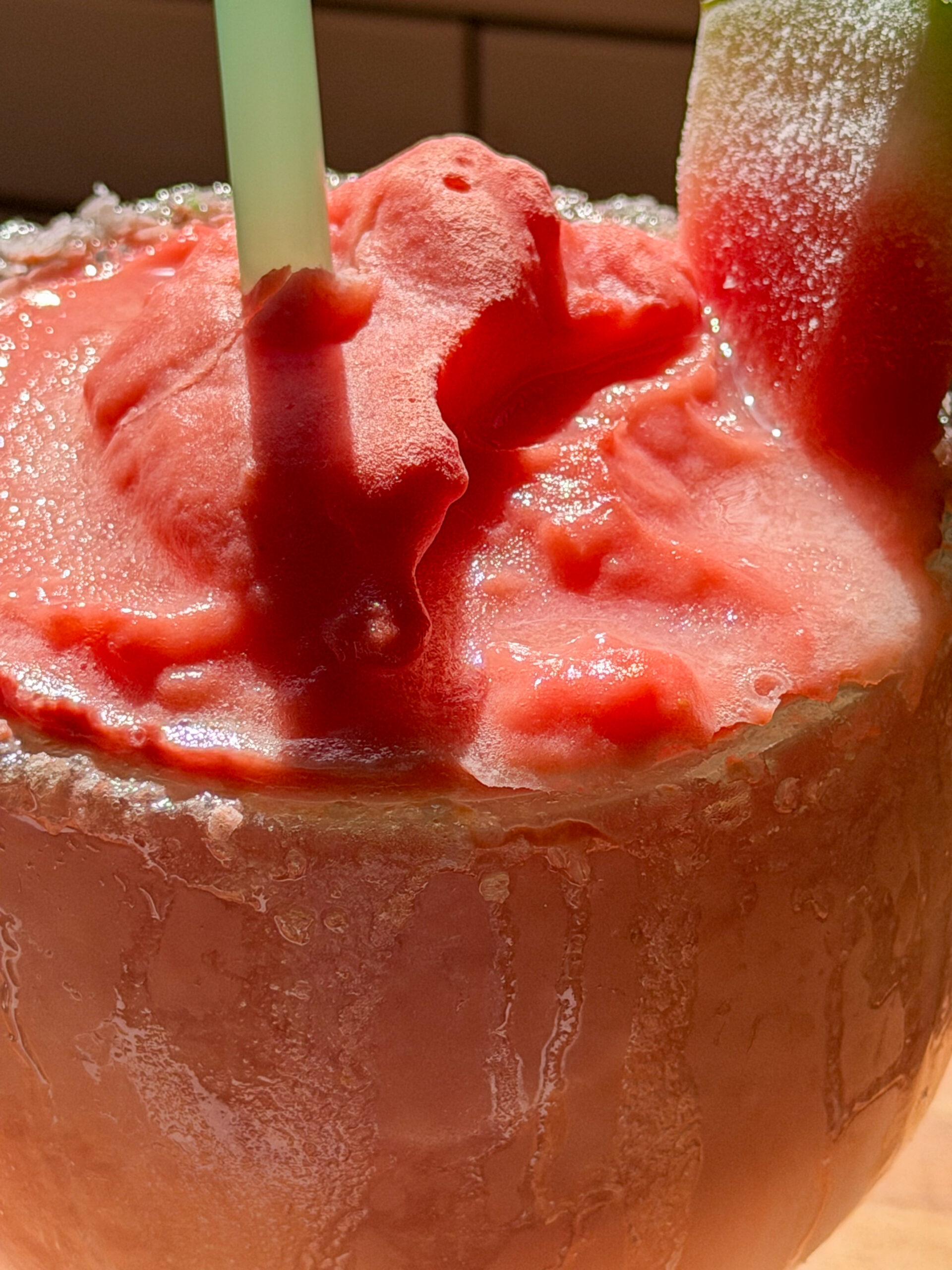 Dipping a glass rim into simple syrup and green salt for a watermelon margarita mocktail